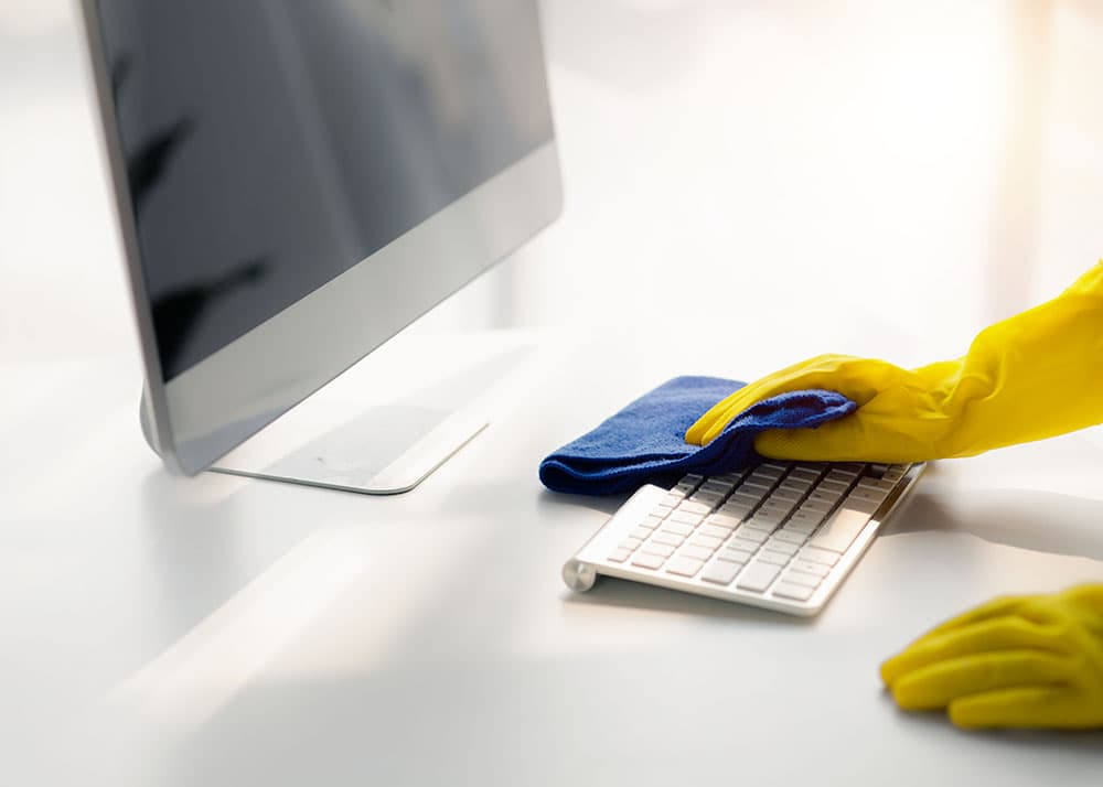 Fachgerechte EDV-Reinigung in Hamburg: Reinigungskraft säubert schonend eine Tastatur und einen Monitor mit einem Mikrofasertuch an einem modernen IT-Arbeitsplatz