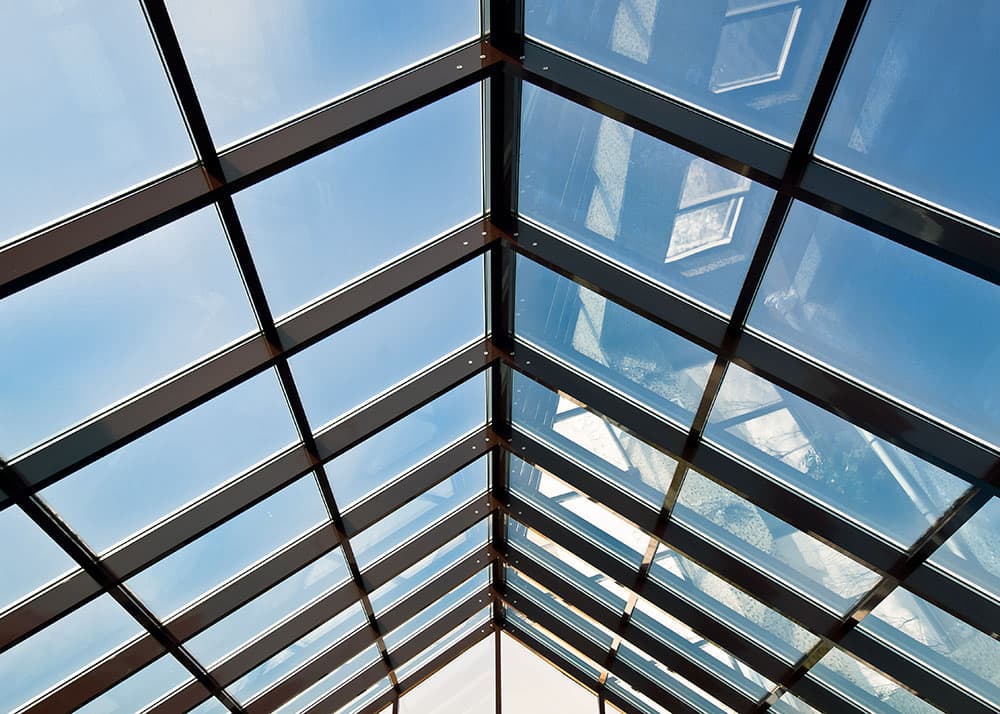 Kristallklare Glasdachreinigung in Hamburg: Freier Blick in den blauen Himmel durch ein perfekt gereinigtes Steildach mit schwarzen Rahmenelementen nach dem Oxonio-Service