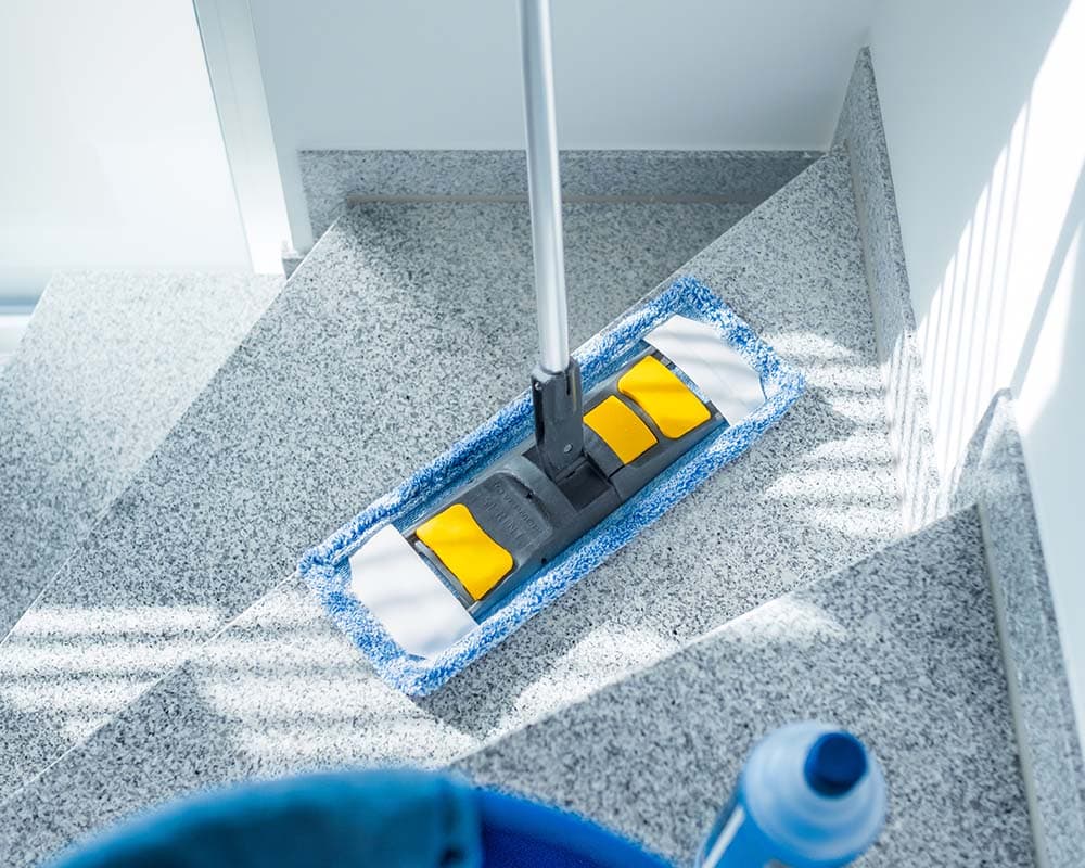 Professionelles Equipment für die Gebäudereinigung in Hamburg: Breitwischgerät, Reinigungsmittel und Eimer einsatzbereit auf einer Treppenstufe