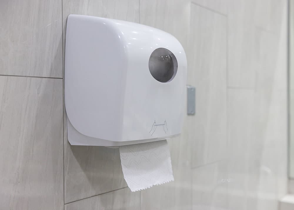 Weißer Papierhandtuchspender an einer gefliesten Wand – zuverlässige Nachfüllung von Verbrauchsmaterial im Rahmen der Unterhaltsreinigung in Hamburg
